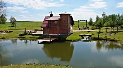 a small wooden cabin on a pond with a bridge at Laukupės sodyba in Rokiškis