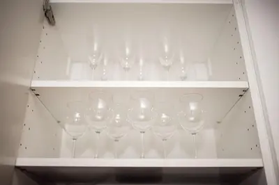 a row of wine glasses in a white cabinet at Crown Apartment in Ukmergė