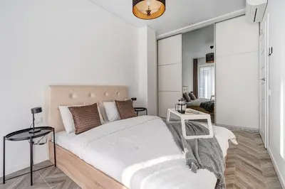 a white bedroom with a bed and a table at cohost I New Bastėja Life Apartments w-Garage Prkg & Self Check-in in Vilnius