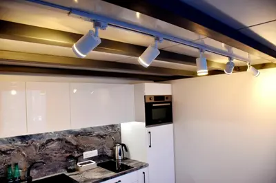 a kitchen with white cabinets and lights on the ceiling at Familia Apartments in Vilnius