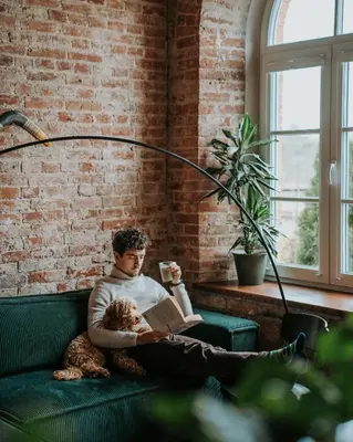 a man sitting on a couch with a dog and a book at Traukinių namai #1 in Švenčionėliai