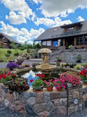 a garden with a fountain and flowers in front of a house at Viesu vila Trakai ,su ežero pakrante in Meiluškės