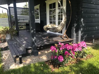 a front porch of a house with a swing and flowers at Atostogų namelis Laukys in Druskininkai