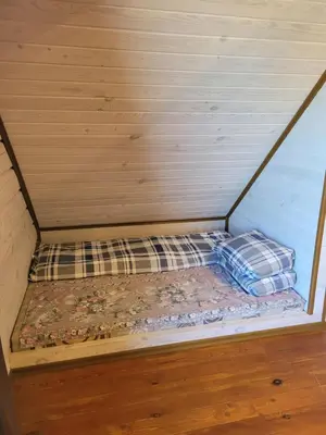a small bed in a room with a wooden wall at Nuomojama sodyba Rokiškio rajonas , Aukštakalnių kaimas ,Ežero gatvė 2 in Kuosiai