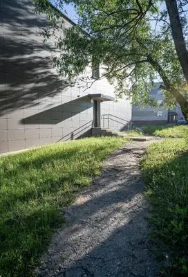 a dirt path next to a building with a tree at Šviesos Apartamentai in Anykščiai
