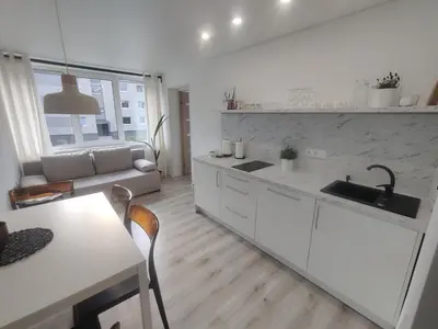 a white kitchen with a sink and a table at Šviesos Apartamentai in Anykščiai