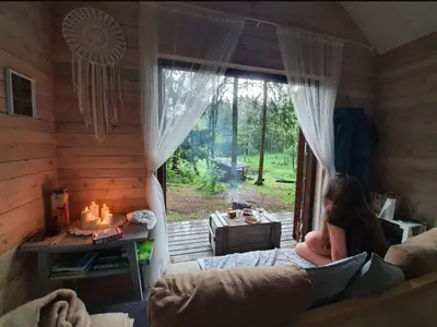 a woman sitting on a couch in a room with a window at Private cosy forest cabin in Inturkė