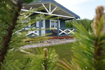 a blue cottage with a porch in a yard at R&M Resort in Petkėniškės