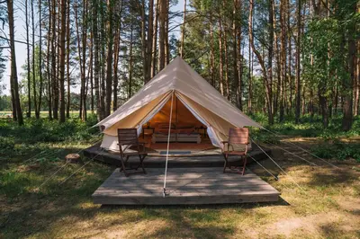 a tent with chairs on a wooden platform in a forest at Natur Camp Glamping Birštonas in Birštonas