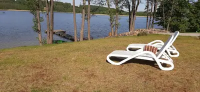 a white lounge chair sitting on the grass by the water at Vila Galadusis prie ežero in Lazdijai