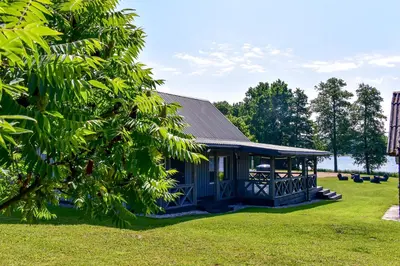 a blue house with a porch in the grass at Sodyba Pivašiūnuose ant ežero kranto in Pivašiūnai