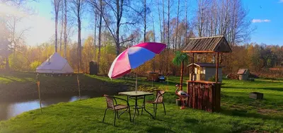 a table and chairs with an umbrella next to a pond at Glamping in - luxury tent in Šunupis