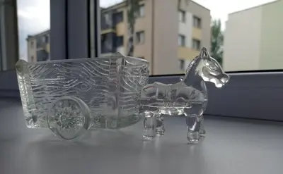 a clear glass horse pulling a cart on a table at TIMO butas in Druskininkai