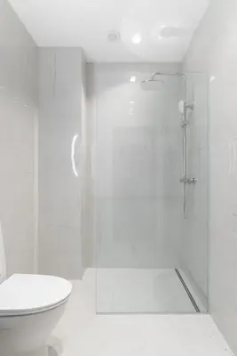 a white bathroom with a shower and a toilet at Brand New and Modern 1BDR Apartment in Vilnius
