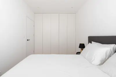 a bedroom with a bed with white sheets and a door at Brand New and Modern 1BDR Apartment in Vilnius