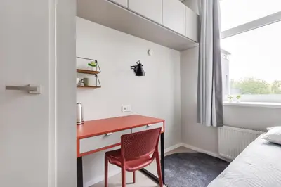 a red desk in a bedroom with a bed and a window at Youston self check-in coliving Vilnius in Vilnius
