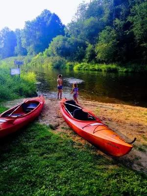 a man and a child standing next to two canoes on a river at Atostogų namelis-pirtis Prie upės in Anykščiai