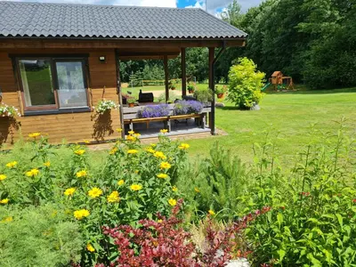 a wooden gazebo in a garden with flowers at Atostogų namelis-pirtis Prie upės in Anykščiai