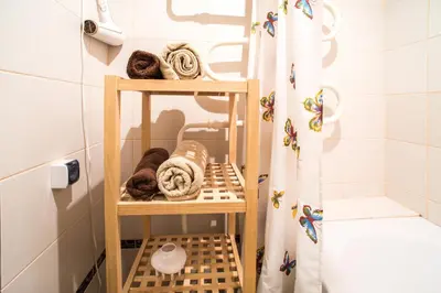 a bathroom with a wooden shelf with towels and a shower curtain at Apartment Stay In in Druskininkai