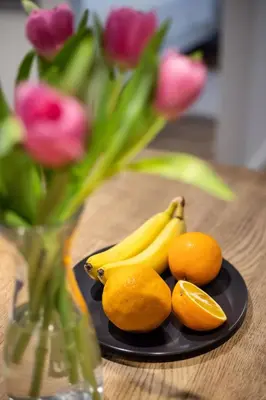 a plate with bananas oranges and a vase with flowers at City Center Sanctuary Modern Business-Class Studio with Free Parking in the Heart of Vilnius in Vilnius