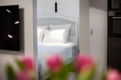 a white bed with a white pillow and pink flowers at City Center Sanctuary Modern Business-Class Studio with Free Parking in the Heart of Vilnius in Vilnius