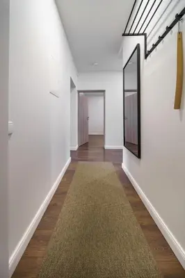 a hallway with white walls and a rug and a mirror at Nica Apartment in Šiauliai