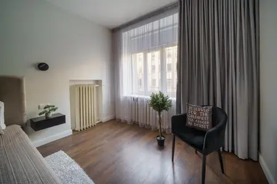 a bedroom with a bed and a chair and a large window at Nica Apartment in Šiauliai