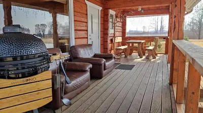 a porch of a cabin with a grill and a chair at Padvarių sodyba ant tvenkinio kranto su pirtimi in Šiupieniai