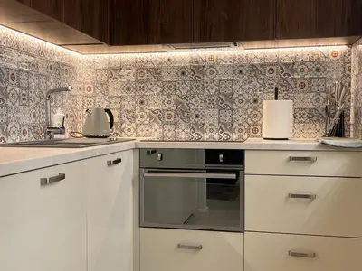 a kitchen with white cabinets and a tile wall at Luxuria Modern Apartments - Self Check-in in Šiauliai