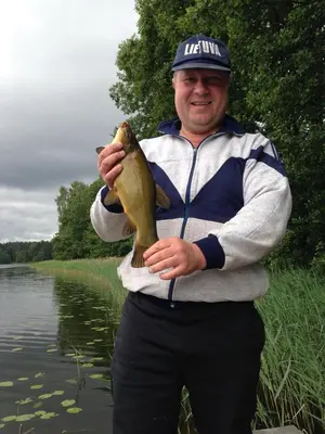 a man holding a fish in front of a body of water at Pirtelė Arjola in Kaltanėnai