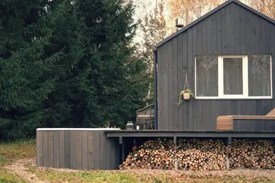 a black house with a pile of fire wood at Hand made Off Grid forest Cabin Luna in Luksine