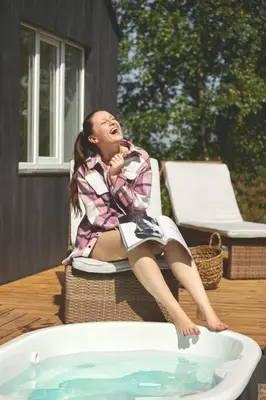 a woman sitting on a chair next to a tub at Hand made Off Grid forest Cabin Luna in Luksine