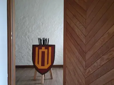 a shield on a stand next to a wooden door at Sodyba PILIAKIEMIS in Kurkliškės