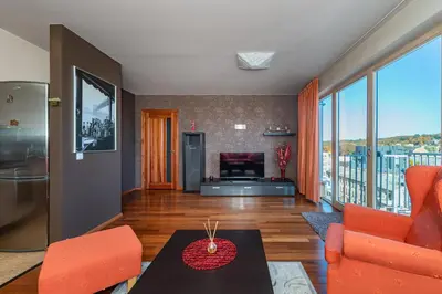 a living room with orange chairs and a couch and a table at Panoramic city centre apartment by Polo Apartments in Kaunas