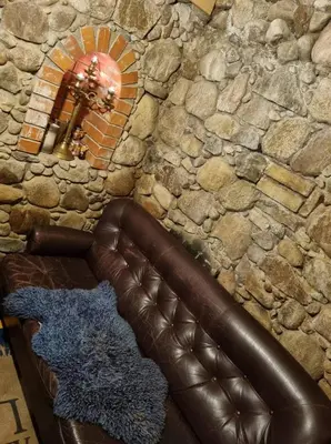 a leather couch in front of a stone wall with a mirror at ODM&A apartment in Vilnius