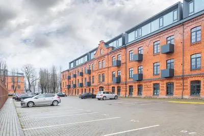 a large brick building with cars parked in a parking lot at Shanti barracks apartment by Polo Apartments in Kaunas