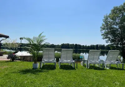four white chairs sitting in the grass near a lake at AGUONA ROYAL OASIS in Molėtai