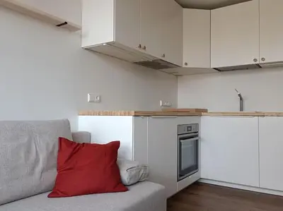 a kitchen with white cabinets and a red pillow on a couch at Stylish Studio in Central Vilnius II in Vilnius