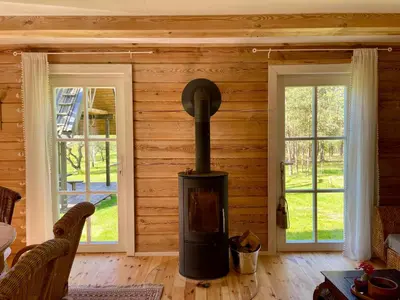 a woodburning stove in a living room with two windows at Holiday homestead Camp of Forest Souls in Masališkės