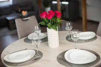 a table with white plates and red roses in a vase at Petro studija in Kaunas