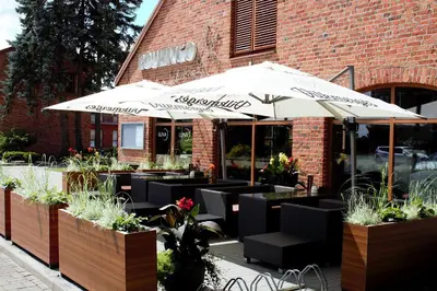 a restaurant with tables and umbrellas in front of a building at LUNA Marijampole in Marijampolė