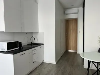 a white kitchen with a table and a microwave at Arena apartment in Kaunas